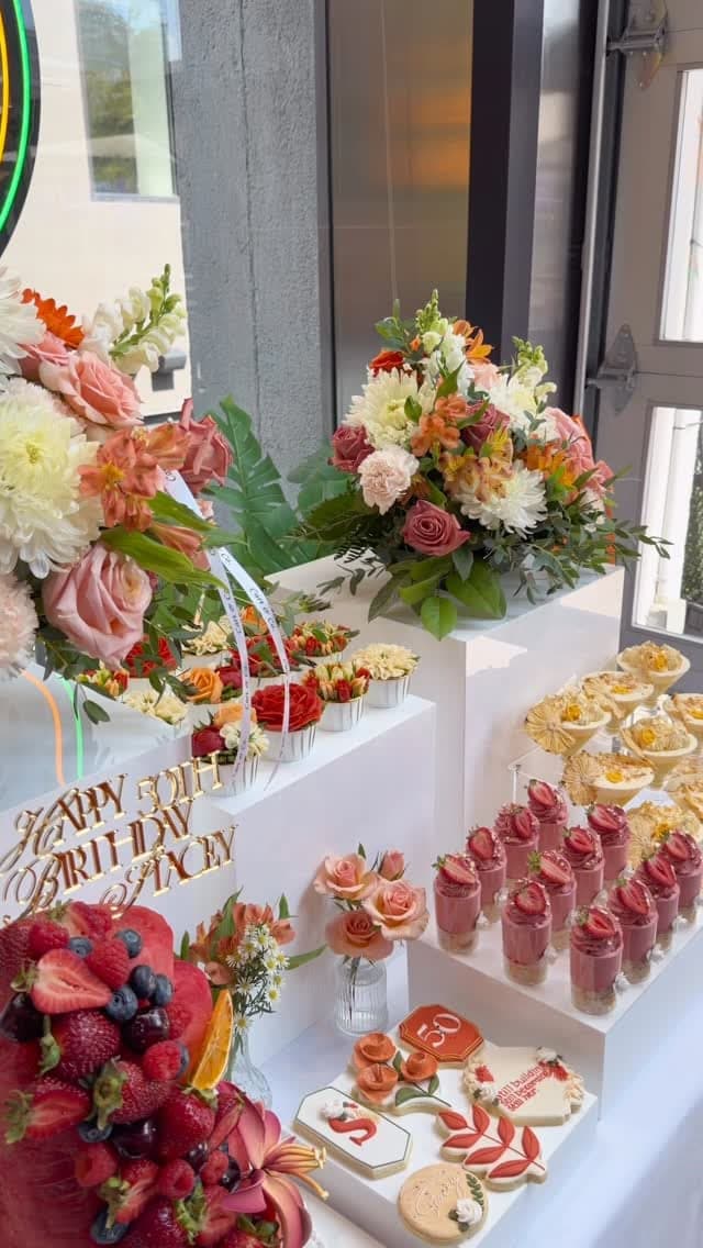 Custom '50th Birthday' signage beside a styled dessert display with fruit tarts, berry mousse cups and fresh florals