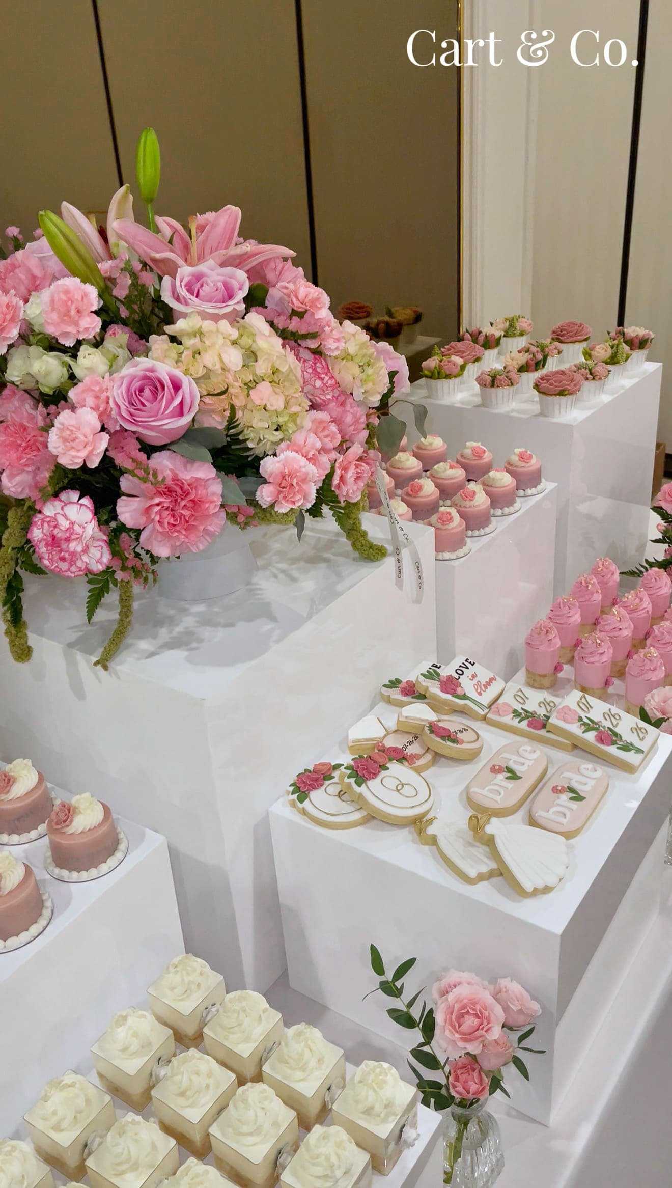 Pink bridal shower dessert table with 'bride' cookies, rose mini cakes and a lily and carnation centerpiece