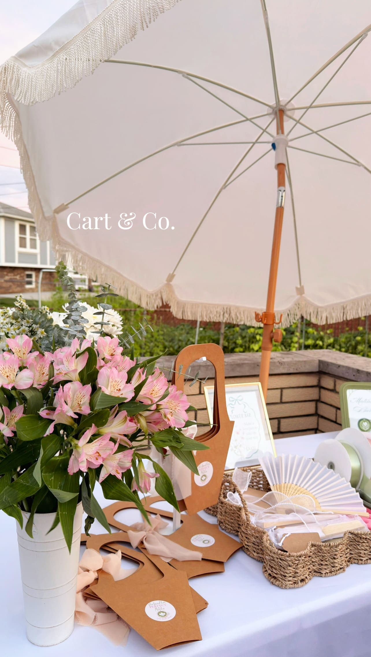 Flower bar styling props — a market umbrella, kraft paper totes, hand fans and ribbon spools — staged for a build-your-own bouquet bar