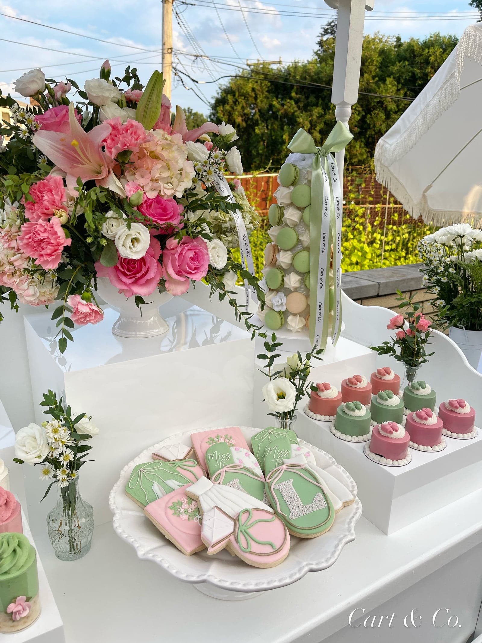 Outdoor bachelorette dessert display with pink and green mini cakes, a ribboned macaron tower and 'Miss to Mrs' cookies styled by Cart & Co.