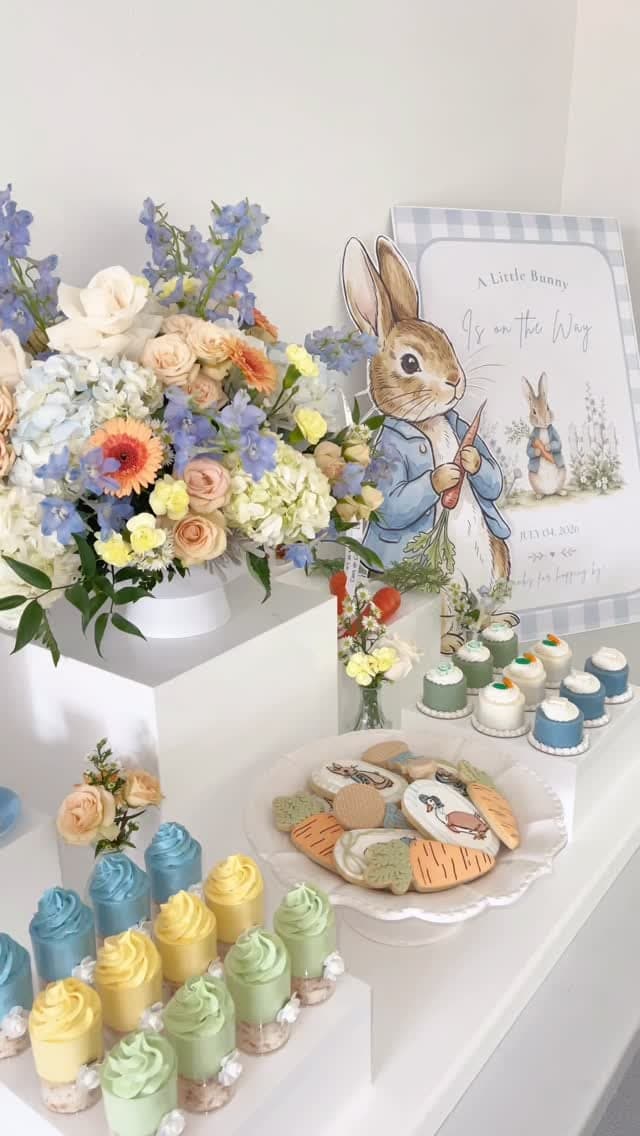 Peter Rabbit-themed baby shower dessert table with custom illustrated signage, coordinated pastel mini desserts and florals