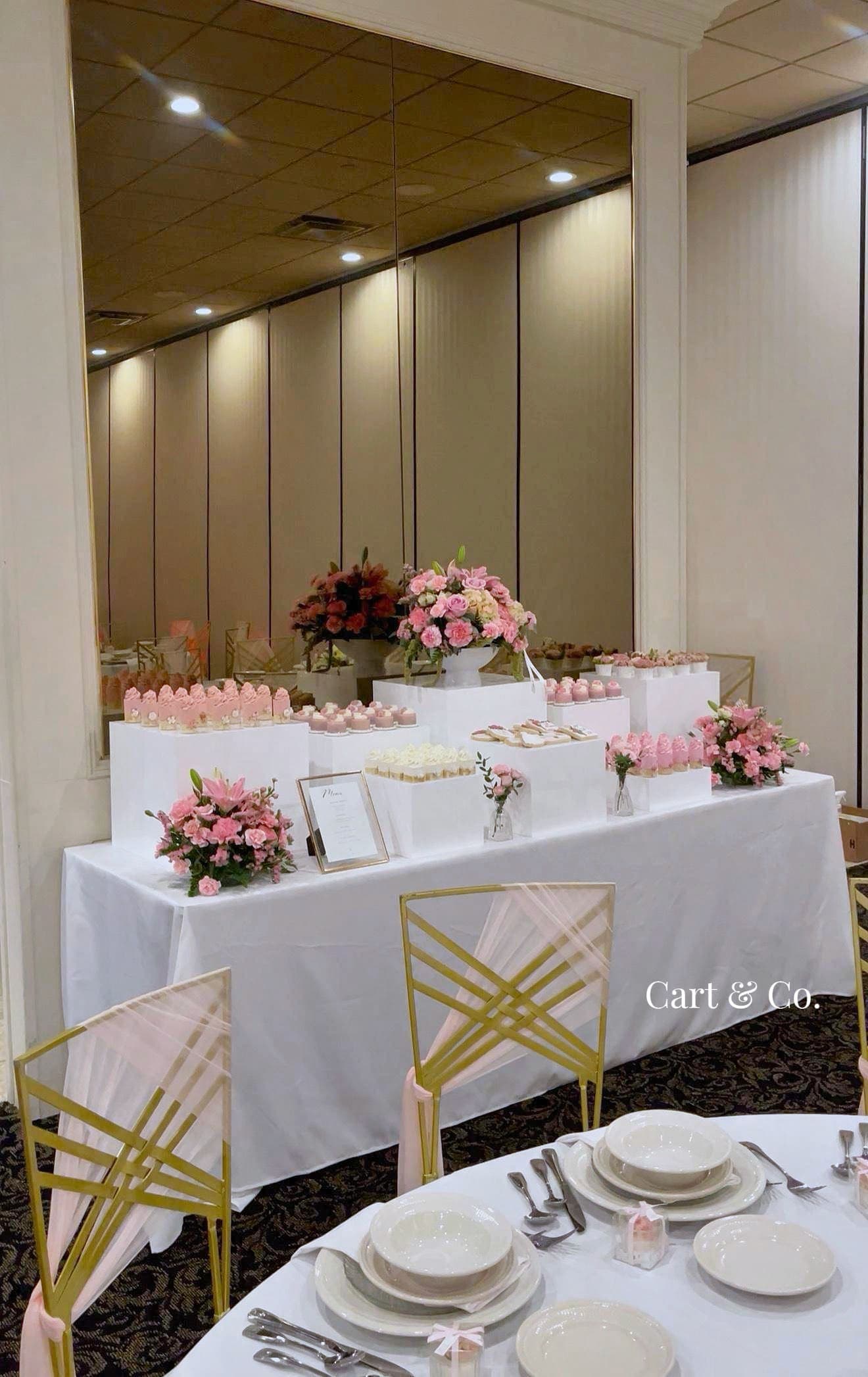 Pink dessert table styled in a gold-mirrored ballroom, with florals, mini cakes and place settings for a reception