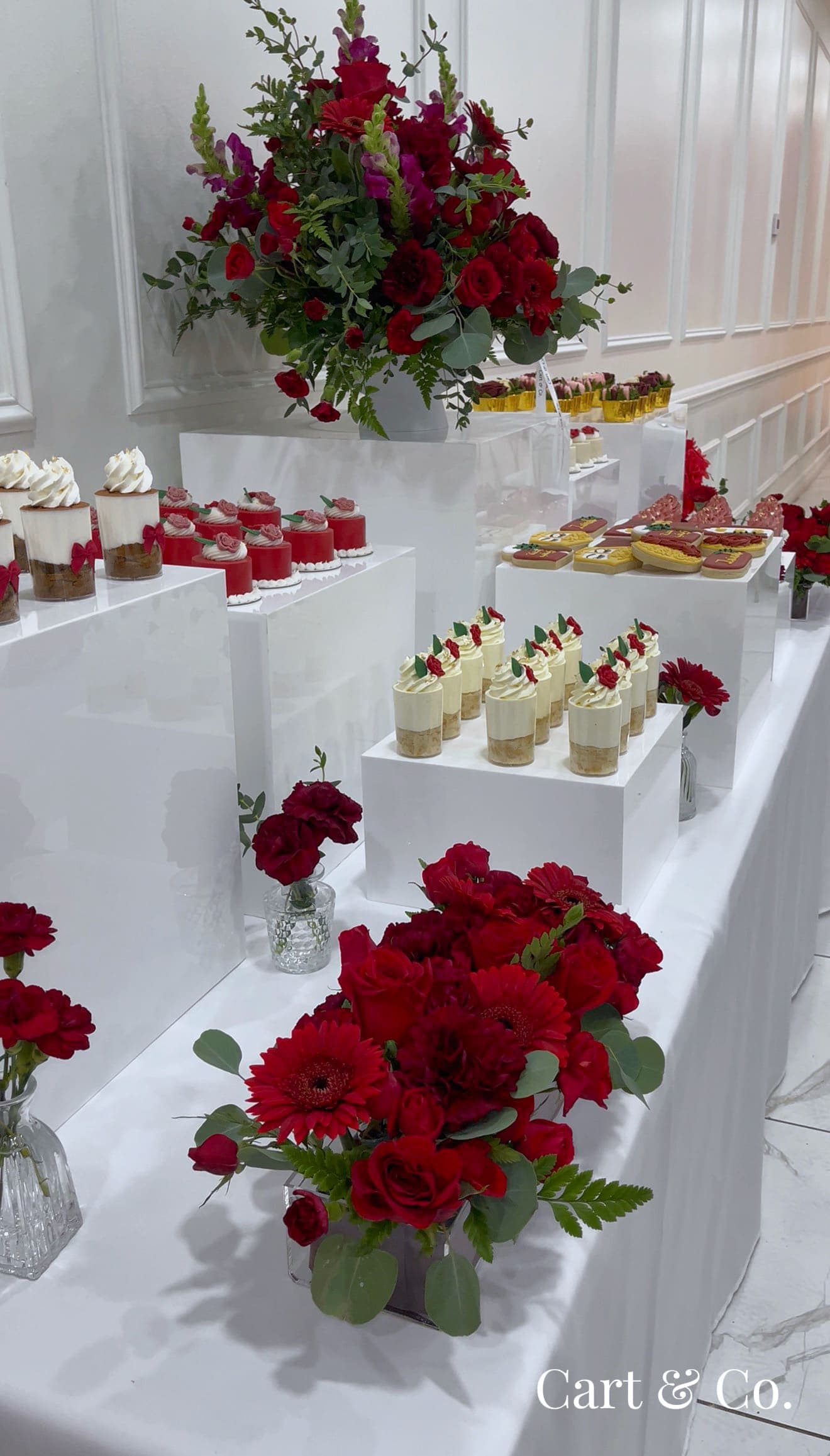 Red rose and gerbera daisy arrangements styled beside red velvet mini cakes and cream mousse cups