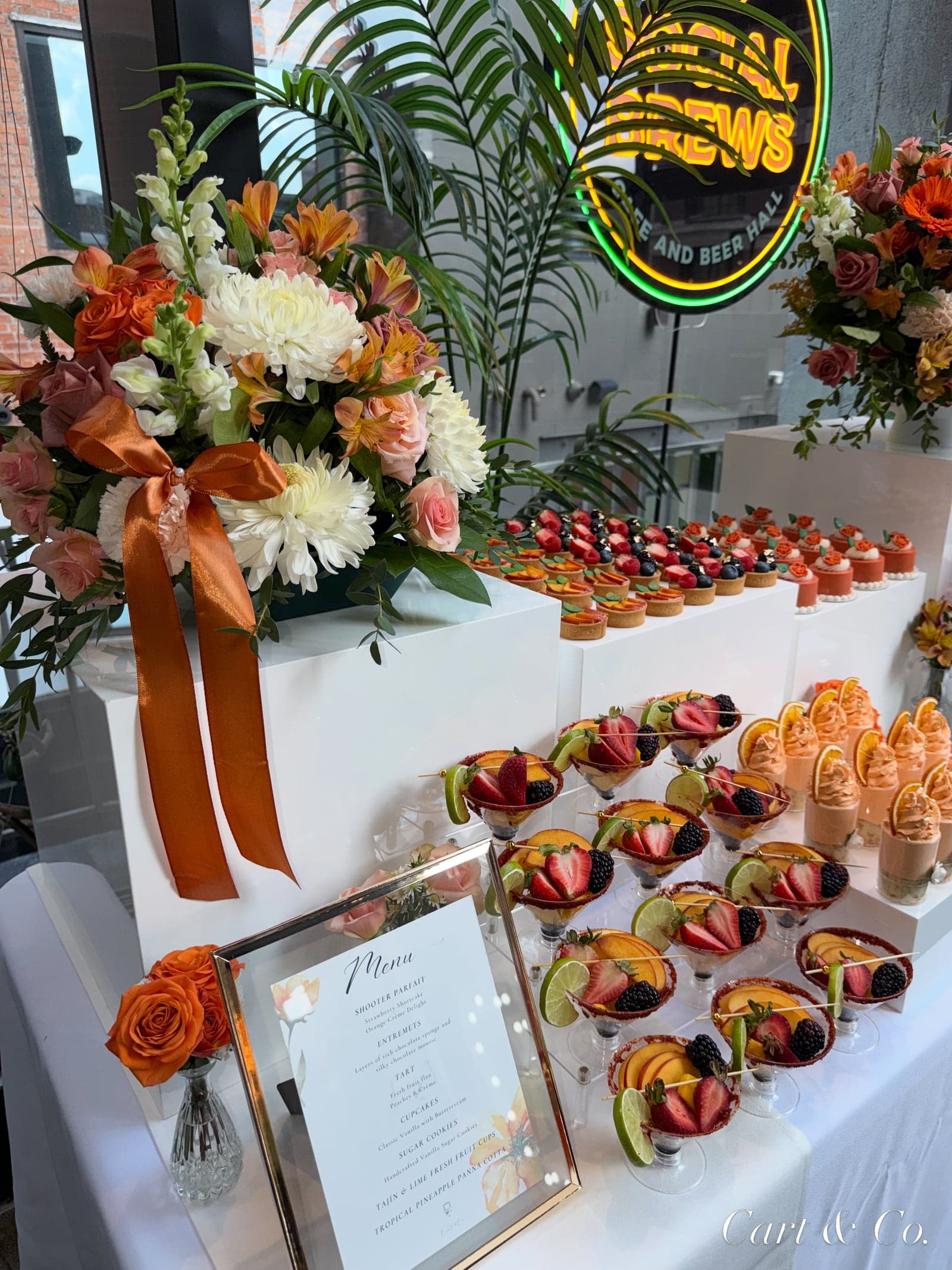 Rooftop grazing table with fruit tarts, tropical florals, and fresh fruit cocktail cups styled by Cart & Co.