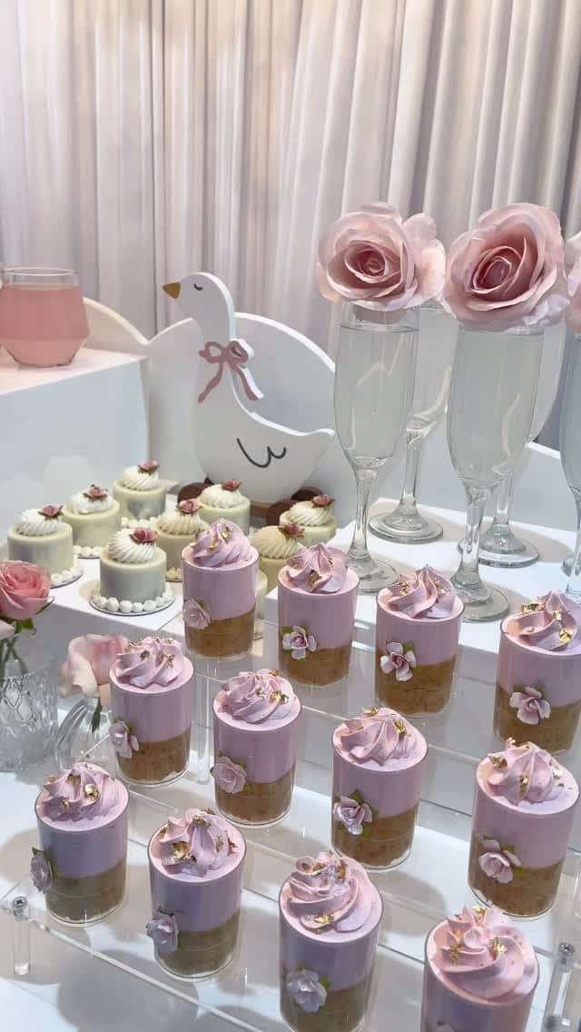Pastel pink dessert cups with gold leaf and sugar flowers, styled with a swan motif and champagne flutes for a baby shower