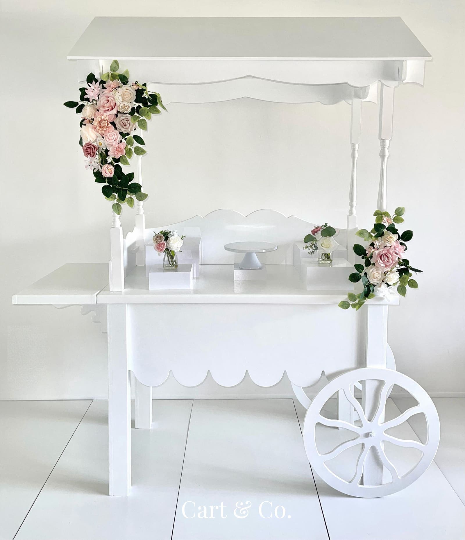 A white Cart & Co. dessert cart with pink and ivory rose swags and a cake stand, studio product photograph