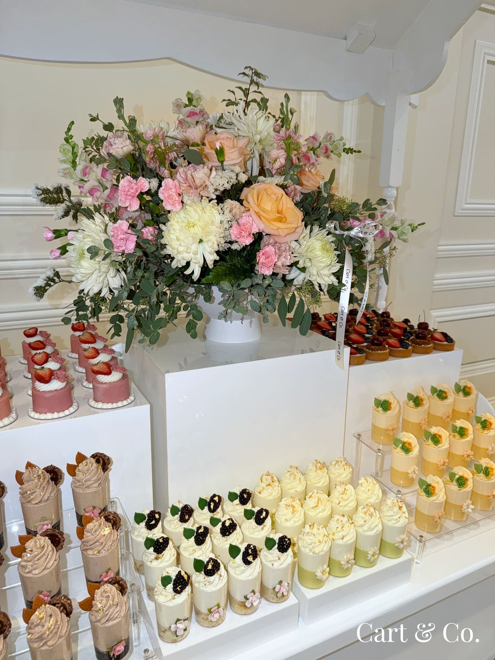 A white rose and dahlia centerpiece beside berry tarts and cream mousse cups, styled on a Cart & Co. dessert table