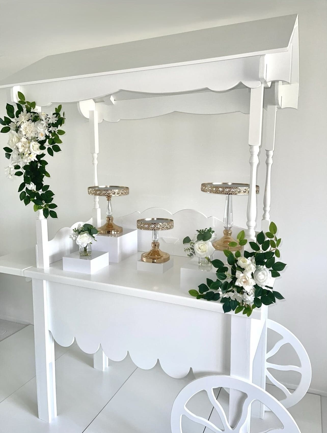 Styled white dessert cart with gold cake stands and lush white floral garlands by Cart & Co.